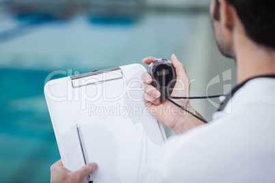 Handsome trainer holding stopwatch and reading clipboard