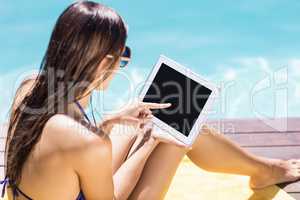 Brunette using tablet poolside