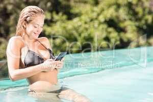 Smiling blonde using smartphone in the pool