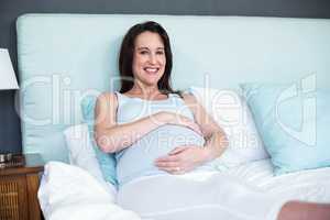 Pregnant woman lying in bed touching belly