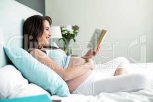 Pregnant woman on bed reading a book