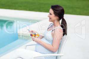 Smiling pregnant woman eating fruit