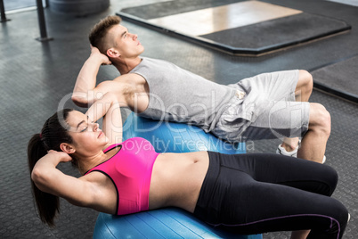 Fit couple doing abdominal crunches on fitness ball