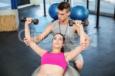 Male trainer assisting woman lifting dumbbells