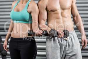 Midsection of fit couple lifting dumbbells