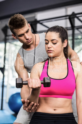 Male trainer assisting woman lifting dumbbells