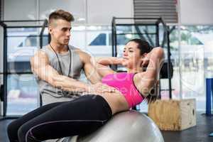 Male trainer assisting woman with sit ups