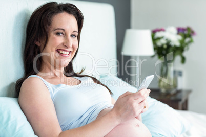 Pregnant woman lying in bed texting