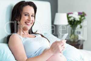 Pregnant woman lying in bed texting
