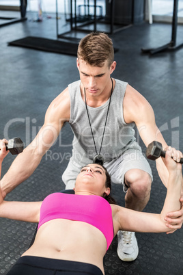 Male trainer assisting woman lifting dumbbell