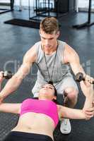 Male trainer assisting woman lifting dumbbell