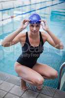 Pretty woman crouching and wearing swim cap and goggles