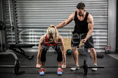 Trainer helping woman with lifting barbell