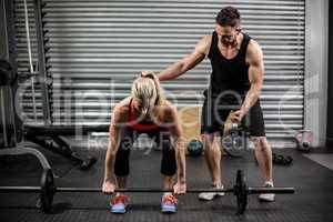Trainer helping woman with lifting barbell