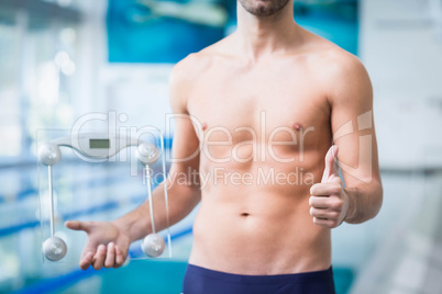 Fit man holding a weighting scale with thumbs up