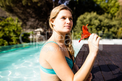 Thoughtful blonde holding red flower