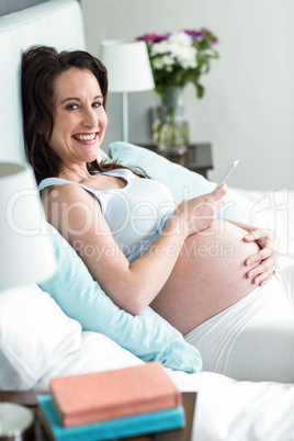 Pregnant woman lying in bed texting