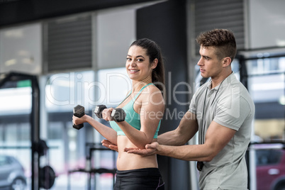 Male trainer assisting woman lifting dumbbells