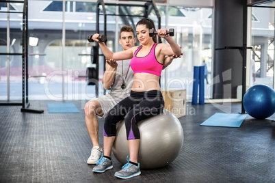 Male trainer assisting woman lifting dumbbells