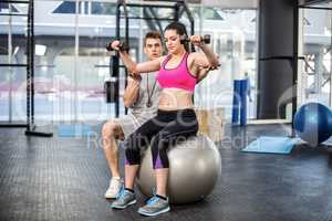 Male trainer assisting woman lifting dumbbells