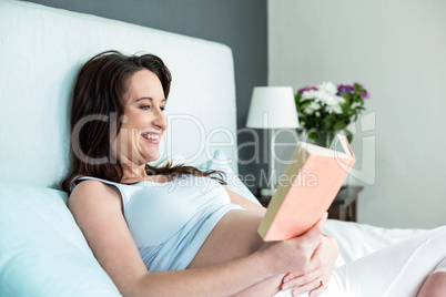 Pregnant woman on bed reading a book