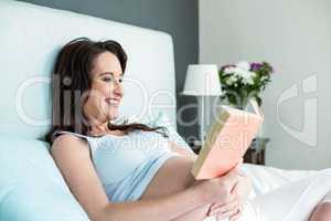 Pregnant woman on bed reading a book