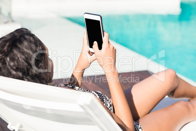 Fit brunette lying on deck chair and using smartphone