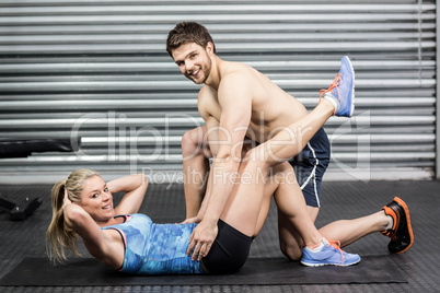 Male trainer assisting woman with sit ups