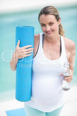 Pregnant woman holding water bottle and mat