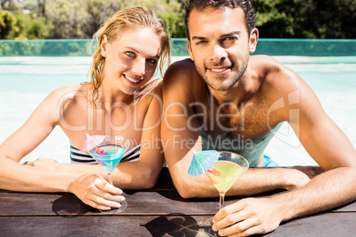 Happy couple leaning on pool edge and holding cocktails
