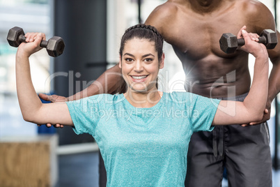 Athletic woman lifting weights helped by trainer