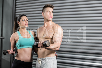 Fit couple lifting dumbbells and looking away