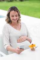 Pregnant woman texting and eating a fruit salad