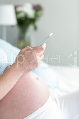 Pregnant woman lying in bed texting