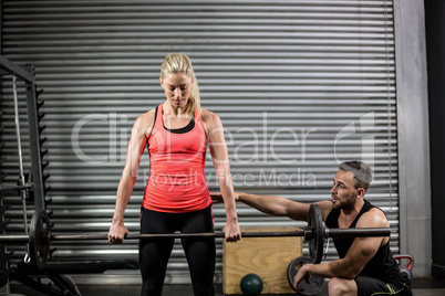 Trainer helping woman with lifting barbell