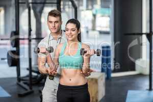 Male trainer assisting woman lifting dumbbells