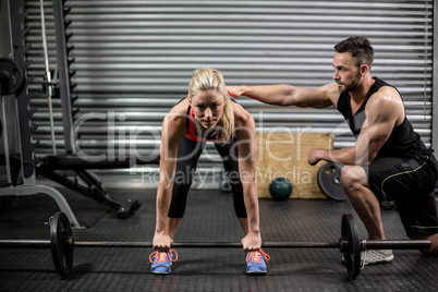 Trainer helping woman with lifting barbell