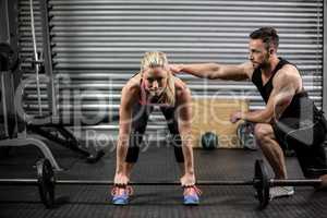 Trainer helping woman with lifting barbell