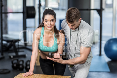 Male trainer assisting woman lifting dumbbells