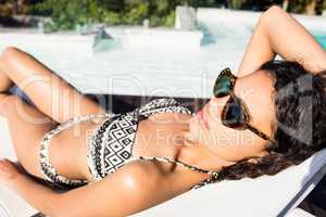 Fit brunette lying on deck chair and using smartphone