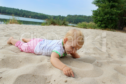 baby lays on the sand at the river