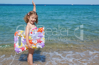 happy little girl standing in the sea with hand up