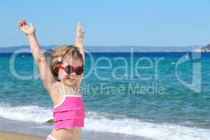 happy little girl with sunglasses and hands up on the beach