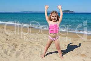 little girl with hands up standing on the beach