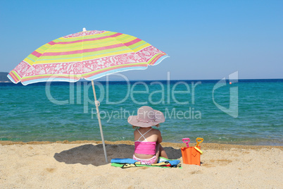 little girl sitting on beach under sunshade
