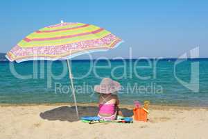 little girl sitting on beach under sunshade