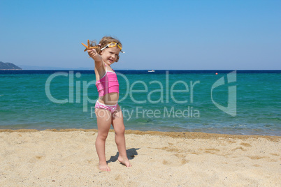 little girl with starfish and goggles on beach