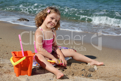 little girl sitting on beach and playing with toys