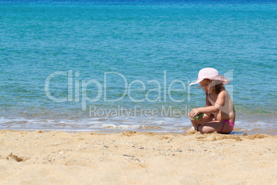 little girl with straw hat playing on the beach