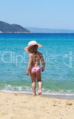 little girl with straw hat walking on beach